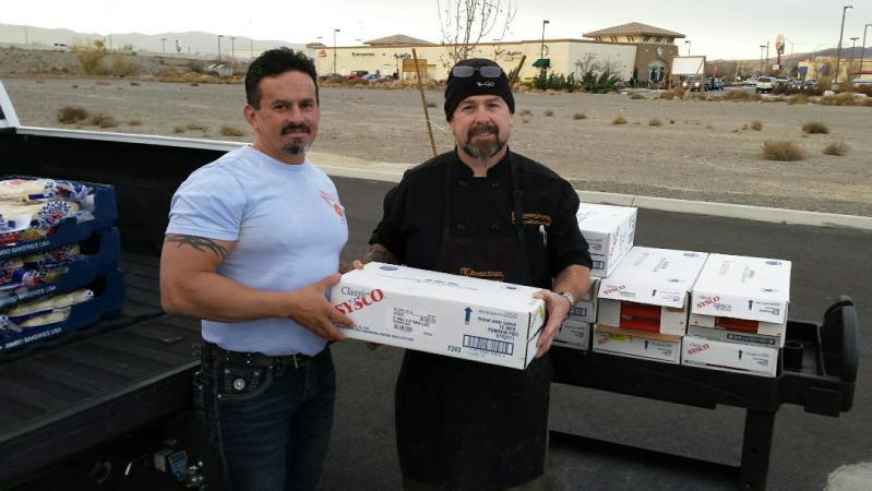 Two men standing in front of a truck with boxes of food.
