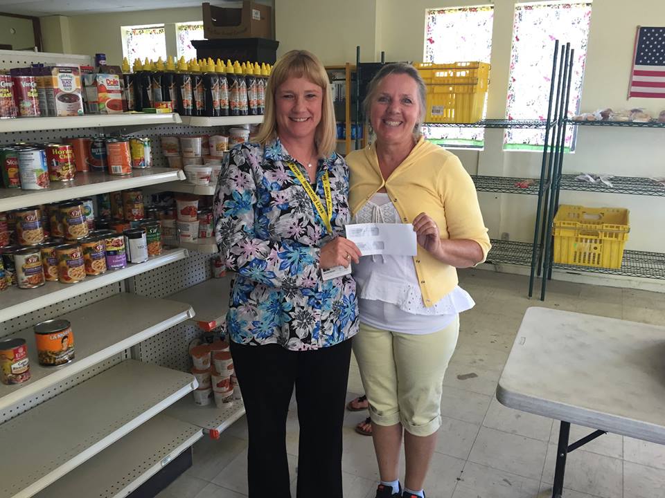 Two women standing in front of a pantry with a check.