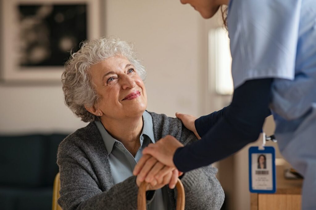 A nurse warmly shakes the hand of a senior woman.