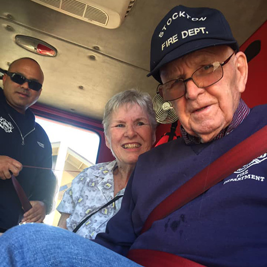 A senior man and woman sitting in the back of a fire truck.